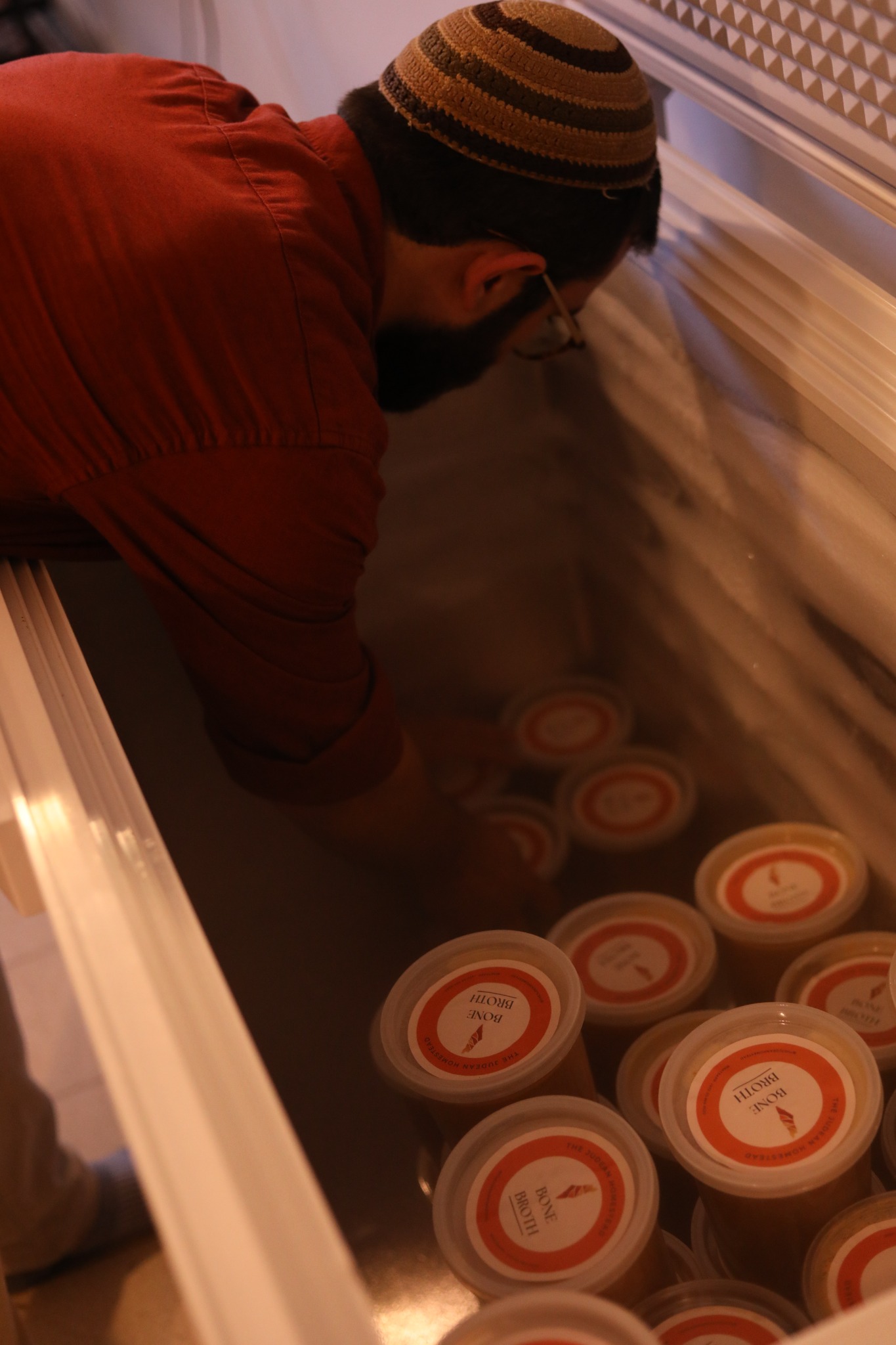 A person arranging containers of bone broth inside a chest freezer.