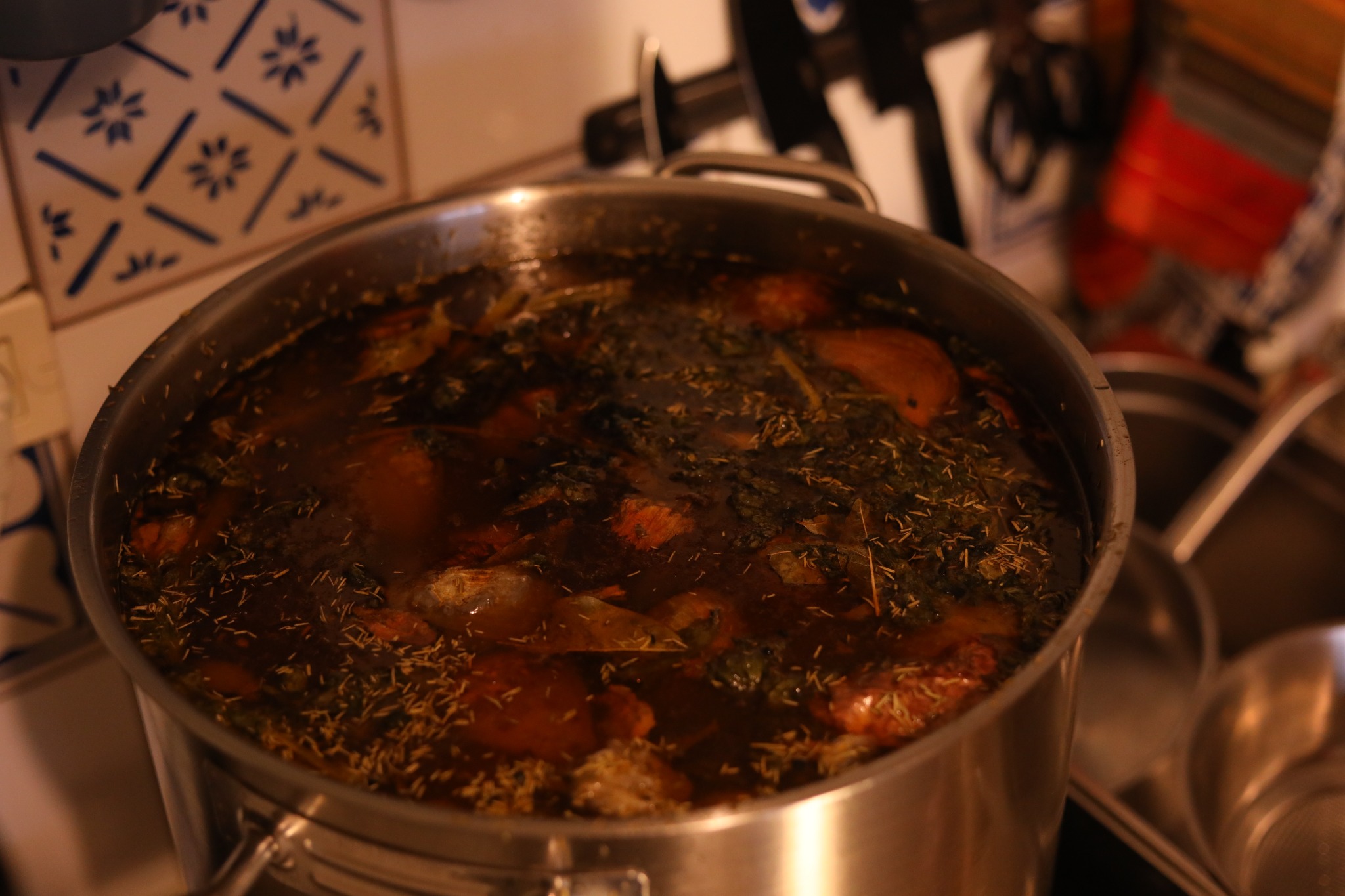 A large stockpot of bone broth simmering with onions and herbs in a home kitchen.